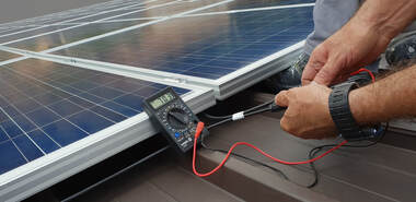 A close up shot of a solar technician using a voltage meter to test the current on a new solar panel on the roof of a modern barn just outside of Davis, CA.