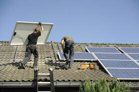 Two solar installers putting solar panels on their mounting racks on a grey Spanish tile roof in Sacramento.