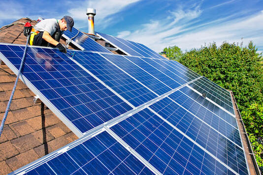 Picture of solar tech installing PV panels on a Sacramento composite rooftop with citrus trees in the background. 